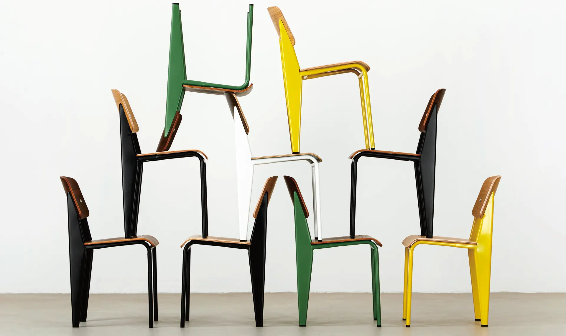 Jean chairs in black, green, white and yellow stacked playfully against a white wall