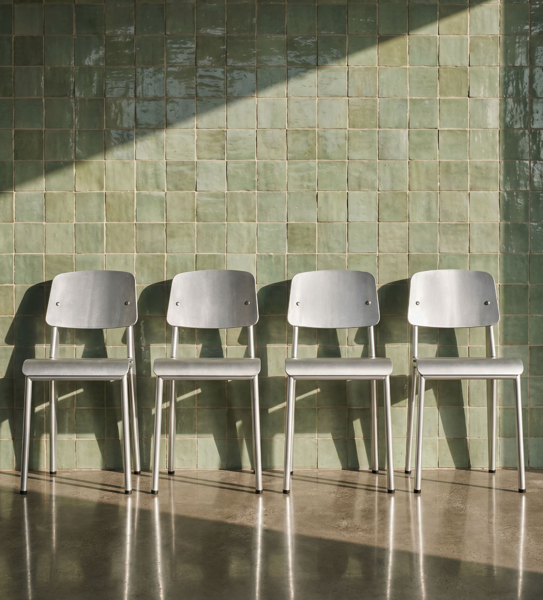Row of aluminum Prouvé chairs against a glazed green tile wall